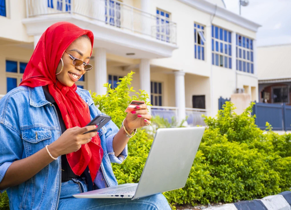 African Female Sitting Outside With Her Laptop Phone Making Payment Online 1